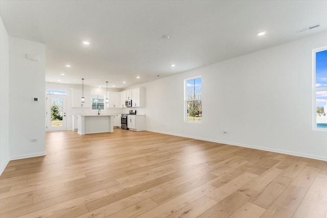 unfurnished living room featuring sink, a healthy amount of sunlight, and light wood-type flooring