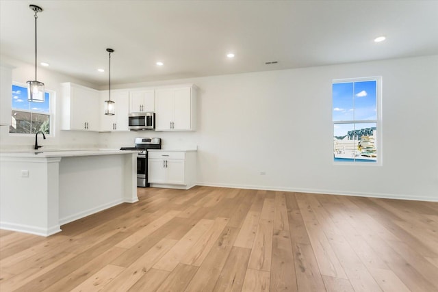 kitchen with a wealth of natural light, decorative light fixtures, white cabinetry, stainless steel appliances, and light wood-type flooring