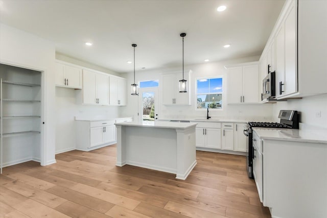 kitchen featuring a kitchen island, appliances with stainless steel finishes, decorative light fixtures, sink, and white cabinets