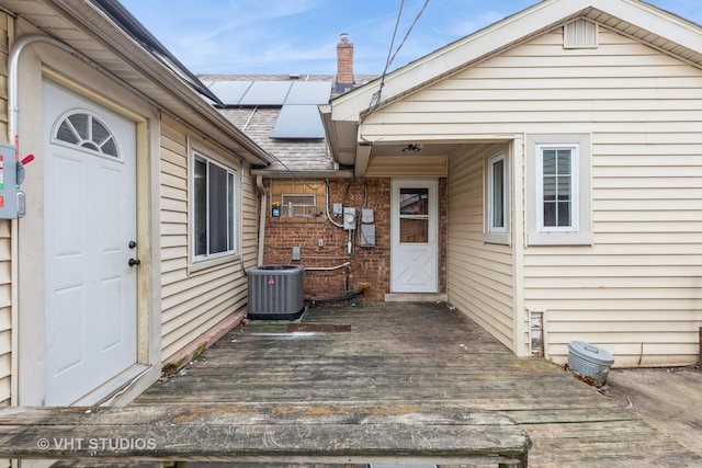 view of exterior entry featuring solar panels, a wooden deck, and central air condition unit