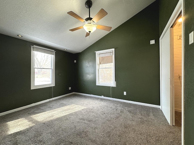 carpeted empty room featuring ceiling fan, a healthy amount of sunlight, vaulted ceiling, and a textured ceiling