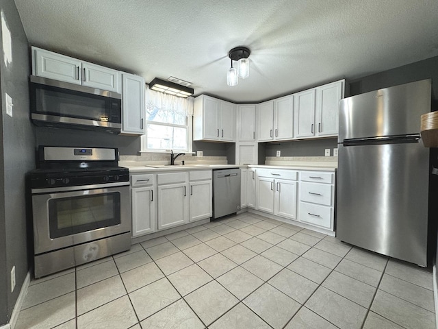 kitchen featuring stainless steel appliances, sink, light tile patterned floors, and white cabinets