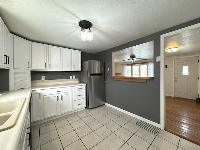 kitchen with light tile patterned floors, a textured ceiling, stainless steel refrigerator, and white cabinets