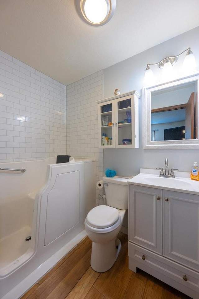 bathroom featuring toilet, hardwood / wood-style flooring, a bath, and vanity