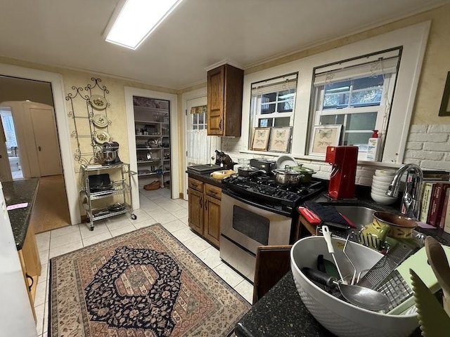 kitchen featuring sink, light tile patterned floors, and stainless steel range oven