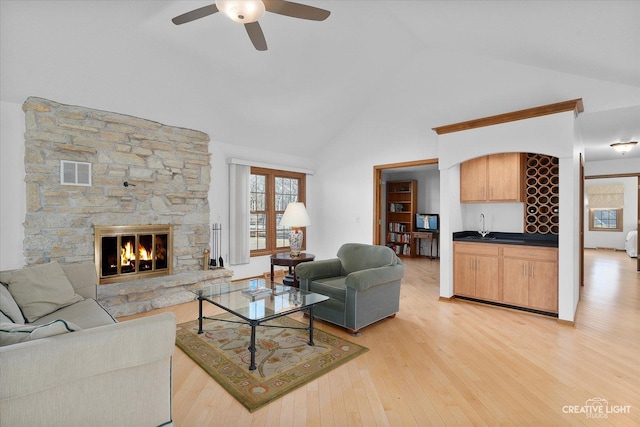 living room with a stone fireplace, lofted ceiling, indoor wet bar, ceiling fan, and light hardwood / wood-style floors