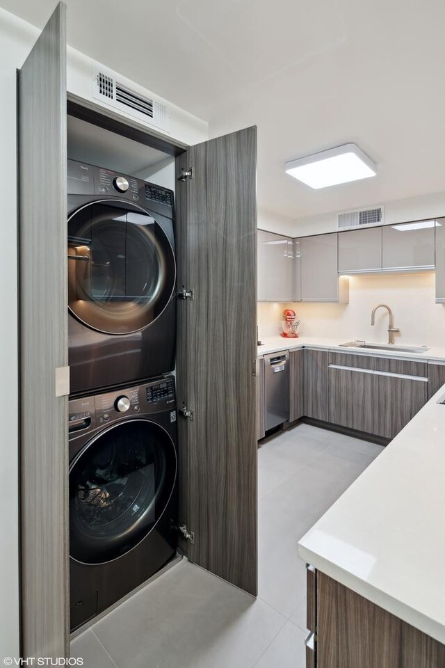 laundry room with light tile patterned flooring, stacked washer and clothes dryer, and sink