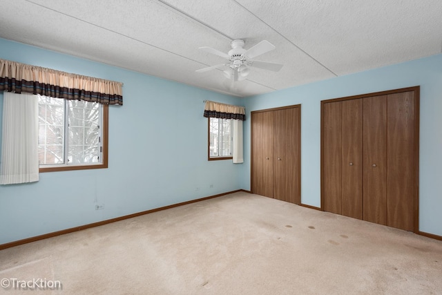 unfurnished bedroom featuring a textured ceiling, ceiling fan, carpet, and multiple closets