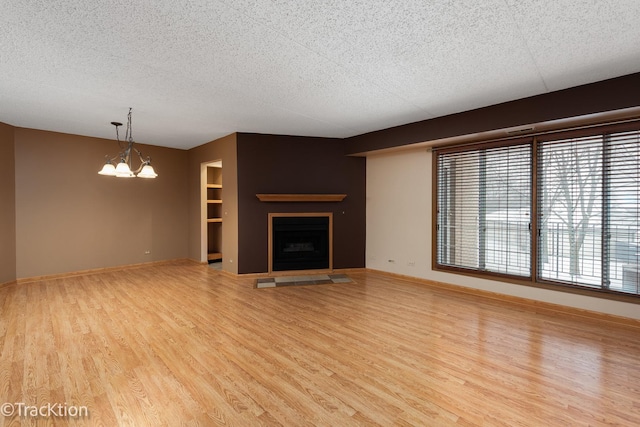 unfurnished living room with an inviting chandelier, light wood-type flooring, and a textured ceiling