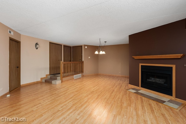 unfurnished living room featuring a notable chandelier, light wood-type flooring, and a textured ceiling