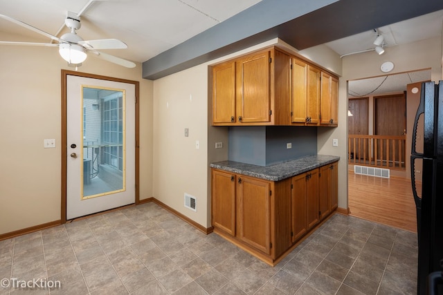 kitchen featuring black fridge, rail lighting, ceiling fan, and dark stone counters