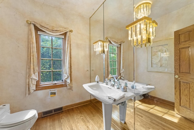 bathroom featuring a healthy amount of sunlight, toilet, wood-type flooring, and a chandelier