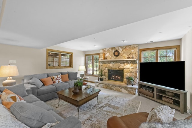 carpeted living room featuring a stone fireplace and a healthy amount of sunlight