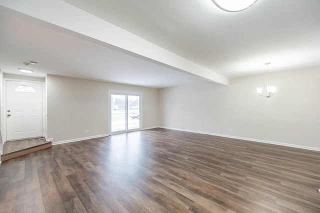 spare room featuring beam ceiling, dark wood-type flooring, and an inviting chandelier