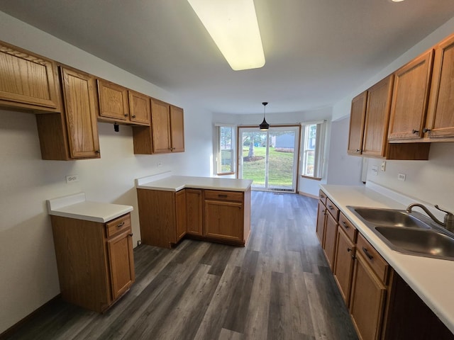 kitchen with decorative light fixtures, kitchen peninsula, sink, and dark wood-type flooring