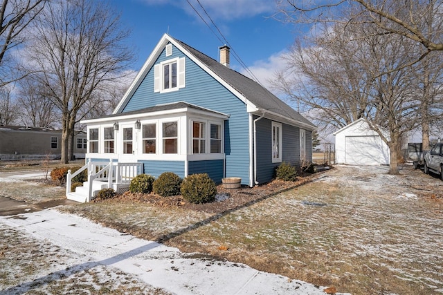 view of snow covered exterior featuring a garage, an outdoor structure, and a sunroom