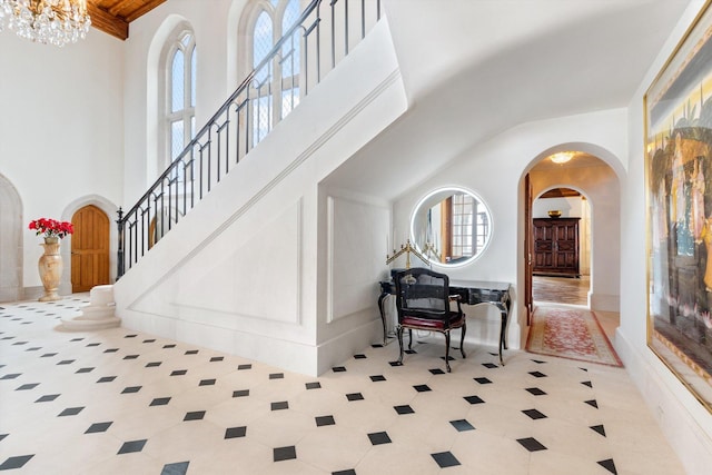 entryway featuring a towering ceiling, light tile patterned flooring, and a notable chandelier