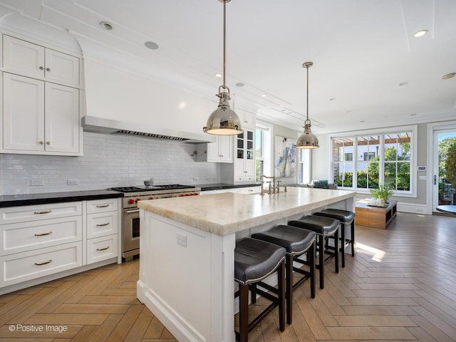 kitchen featuring white cabinetry, parquet flooring, an island with sink, pendant lighting, and luxury stove