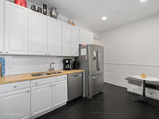 kitchen featuring appliances with stainless steel finishes, butcher block countertops, tasteful backsplash, sink, and white cabinets