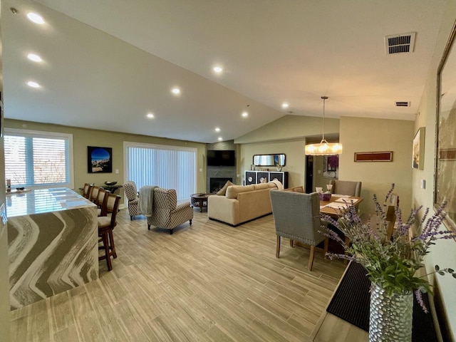 living room with vaulted ceiling, a large fireplace, and light wood-type flooring