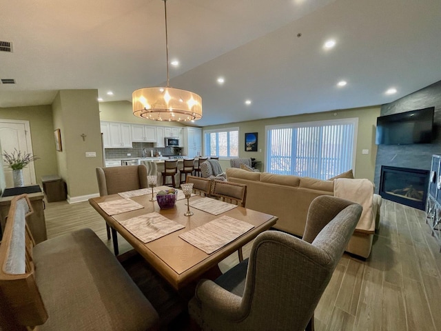 dining area featuring lofted ceiling, a large fireplace, a notable chandelier, and light hardwood / wood-style flooring