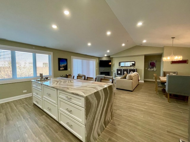 kitchen with light stone counters, white cabinetry, hanging light fixtures, light wood-type flooring, and a kitchen island