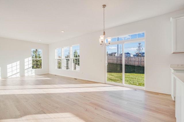 unfurnished dining area with light hardwood / wood-style floors, an inviting chandelier, and a water view