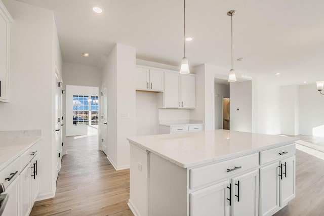 kitchen featuring white cabinetry, a kitchen island, light stone counters, and decorative light fixtures