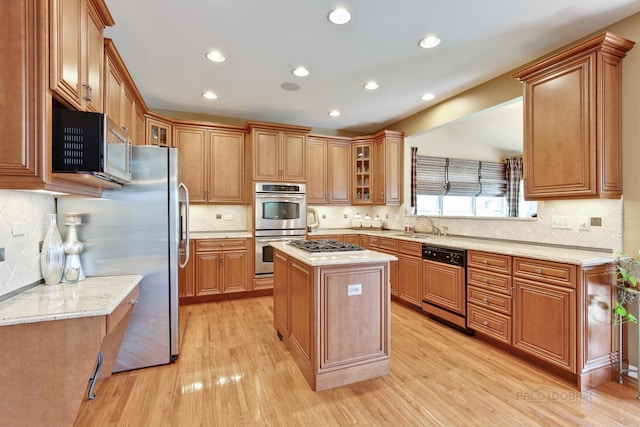 kitchen with a center island, light hardwood / wood-style flooring, decorative backsplash, light stone countertops, and appliances with stainless steel finishes