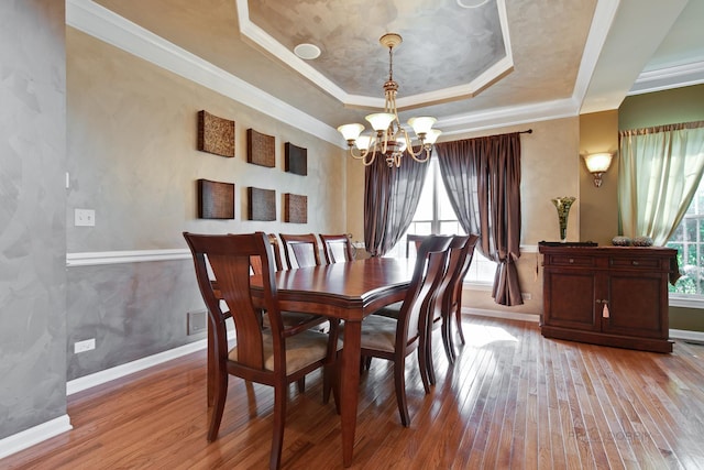 dining space featuring a raised ceiling, light hardwood / wood-style flooring, an inviting chandelier, and ornamental molding