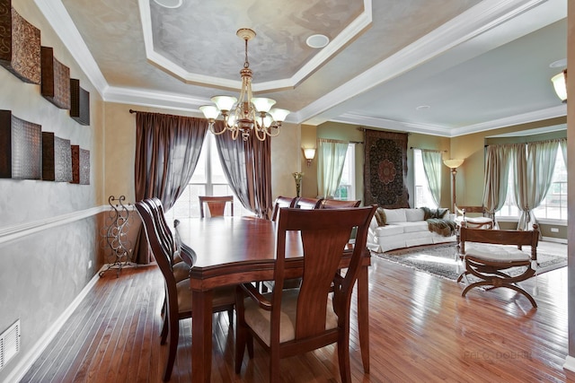 dining room featuring hardwood / wood-style flooring, a raised ceiling, ornamental molding, and an inviting chandelier