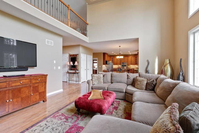 living room with light hardwood / wood-style floors, a towering ceiling, and a chandelier