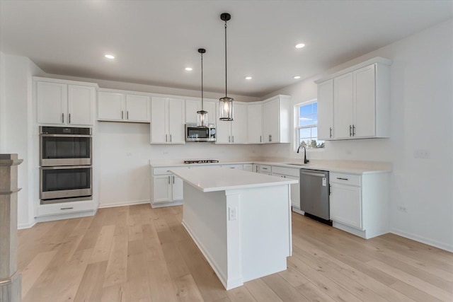 kitchen featuring appliances with stainless steel finishes, pendant lighting, light hardwood / wood-style flooring, a center island, and white cabinetry