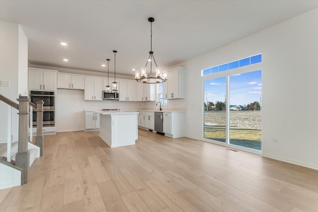 kitchen featuring white cabinets, light wood-type flooring, appliances with stainless steel finishes, decorative light fixtures, and a kitchen island