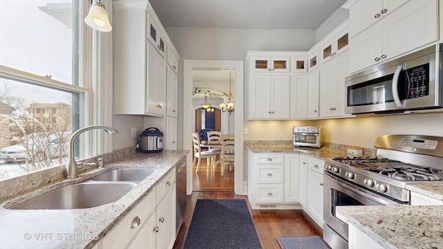 kitchen with pendant lighting, appliances with stainless steel finishes, white cabinetry, sink, and light stone counters