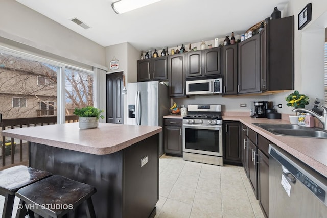 kitchen featuring appliances with stainless steel finishes, a breakfast bar, sink, light tile patterned floors, and a center island