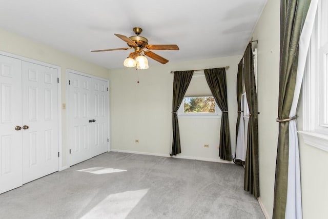 unfurnished bedroom featuring ceiling fan, light colored carpet, and multiple closets