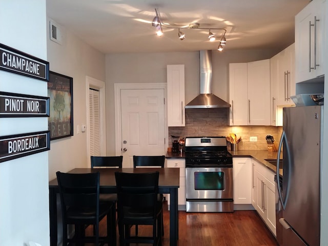 kitchen featuring wall chimney range hood, dark hardwood / wood-style floors, appliances with stainless steel finishes, tasteful backsplash, and white cabinetry