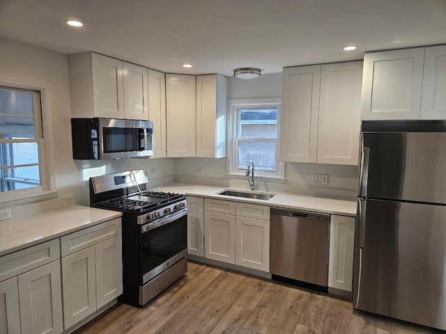 kitchen with white cabinetry, sink, stainless steel appliances, and light hardwood / wood-style flooring