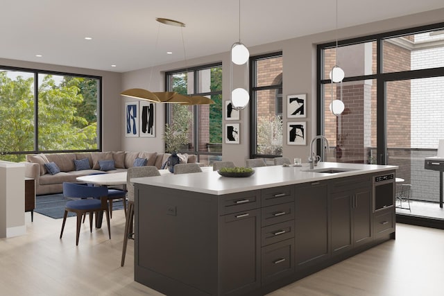 kitchen with decorative light fixtures, a sink, open floor plan, light countertops, and a center island with sink