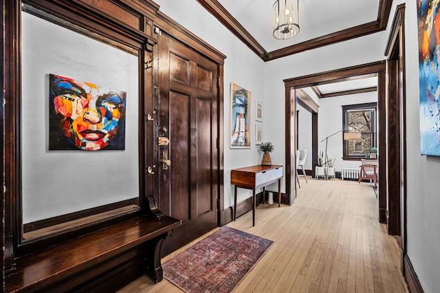 foyer entrance with ornamental molding, light wood-type flooring, a chandelier, and radiator