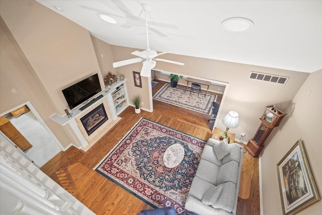 living room with ceiling fan, vaulted ceiling, a tile fireplace, and wood-type flooring