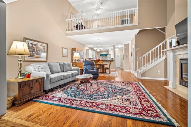 living room with a towering ceiling, a tile fireplace, ceiling fan with notable chandelier, and light hardwood / wood-style flooring