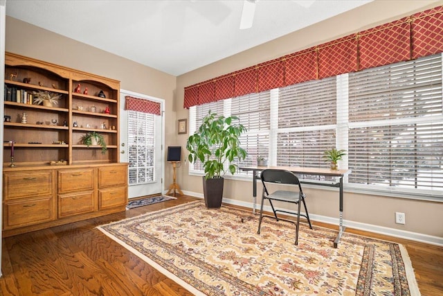 unfurnished office featuring ceiling fan, a healthy amount of sunlight, and dark hardwood / wood-style flooring