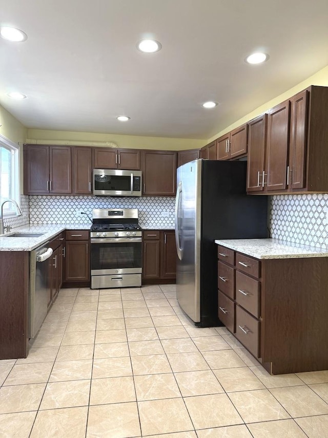 kitchen with light stone countertops, appliances with stainless steel finishes, dark brown cabinetry, sink, and light tile patterned floors