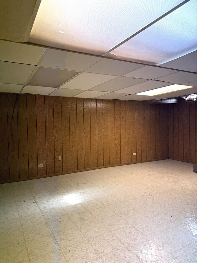 basement featuring wooden walls and a drop ceiling