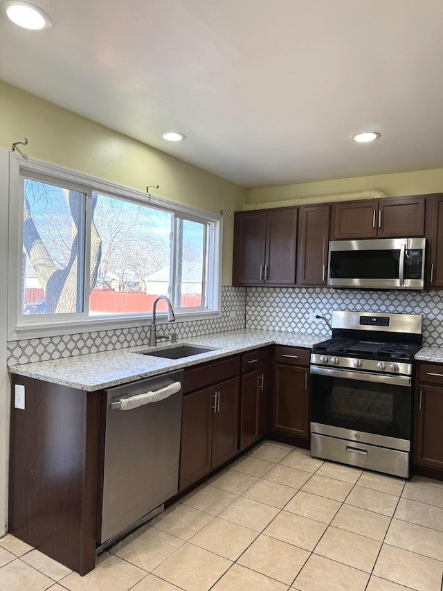 kitchen featuring appliances with stainless steel finishes, light stone counters, dark brown cabinetry, sink, and light tile patterned floors