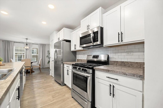 kitchen featuring tasteful backsplash, light hardwood / wood-style floors, pendant lighting, white cabinets, and appliances with stainless steel finishes