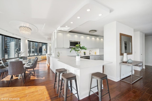 kitchen with hardwood / wood-style floors, a breakfast bar, kitchen peninsula, and appliances with stainless steel finishes