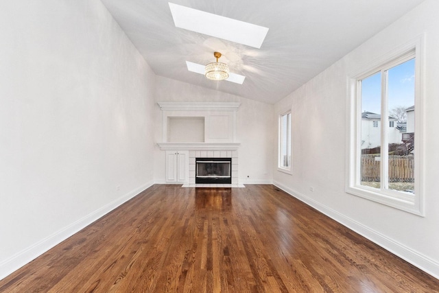 unfurnished living room with dark hardwood / wood-style floors, lofted ceiling with skylight, ceiling fan, and a tiled fireplace